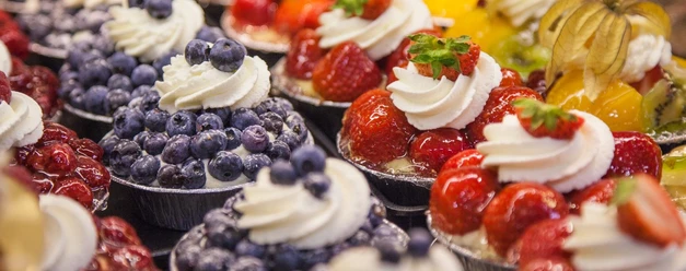 Café Middelberg Nahaufnahme von verschiedenen Törtchen mit Heidelbeeren, Erdbeeren und Physalis, mit einem kleinen Sahnehäubchen oben drauf.