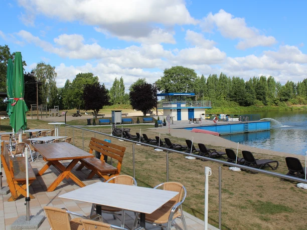 Ein Freibad mit blauen Wasserrutschen und Liegestühlen, umgeben von Grünflächen und Bäumen.