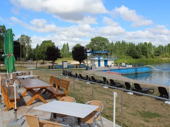 NaturFreibad Eystrup Ein Freibad mit blauen Wasserrutschen und Liegestühlen, umgeben von Grünflächen und Bäumen.
