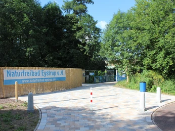 NaturFreibad Eystrup Zugangspfad zum NaturFreibad Eystrup, umgeben von Bäumen, führt zu einem großen Eingangstor.