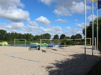 Weißer Sandstrand im Naturfreibad Eystrup mit Volleyballfeld und Wasseraktivitäten im Hintergrund.