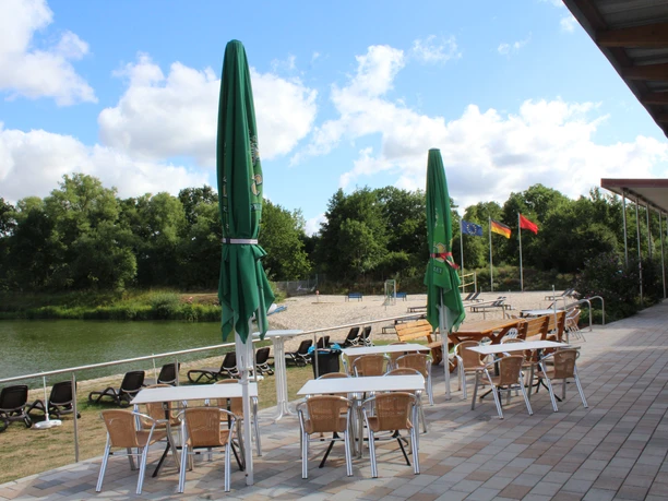 Im Naturerlebnisbad Eystrup stehen auf der Terrasse Tische, Stühle und Sonnenschirme aus hellem Holz.