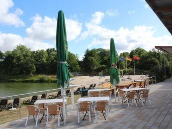 NaturFreibad Eystrup Im Naturerlebnisbad Eystrup stehen auf der Terrasse Tische, Stühle und Sonnenschirme aus hellem Holz.