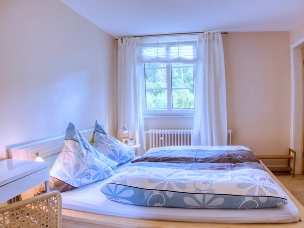 Doppelzimmer Helles Doppelzimmer mit blau gemusterter Bettwäsche und einem Fenster mit Blick ins Grüne.