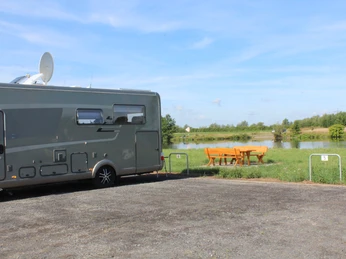 Ein Wohnmobil steht auf einem Stellplatz am Ufer eines Sees, umgeben von grüner Landschaft.