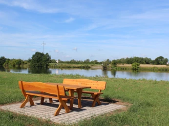 Wohnmobilstellplatz Landesbergen Holztische und Bänke auf gepflasteter Fläche mit Blick auf einen Teich und grüne Landschaft.