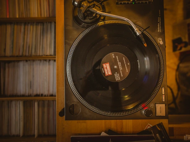 Bahlo Records, Bochum <p>Ein Plattenspieler mit schwarzer Schallplatte, umgeben von Vinylregalen in warmem Licht.</p>