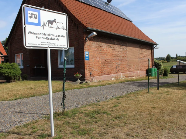 RV parking area with a brick building, an information sign, and a surrounding meadow at Eselweide.
