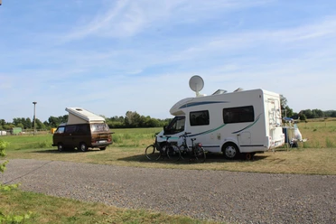 Zwei Wohnmobile stehen auf einer Wiese, mit Fahrrädern und Satellitenschüssel, an einem sonnigen Tag.