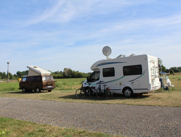 Zwei Wohnmobile stehen auf einer Wiese, mit Fahrrädern und Satellitenschüssel, an einem sonnigen Tag.