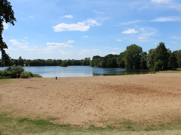 Badesee Lahde Sandstrand am Badesee Lahde mit umgebenem Grün, klarem Himmel und Wolken. Ruhige Wasseroberfläche.