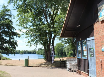 Badesee Lahde Badesee Lahde mit Sandstrand, im Vordergrund ein Kiosk; umgeben von Bäumen und ruhigem See.