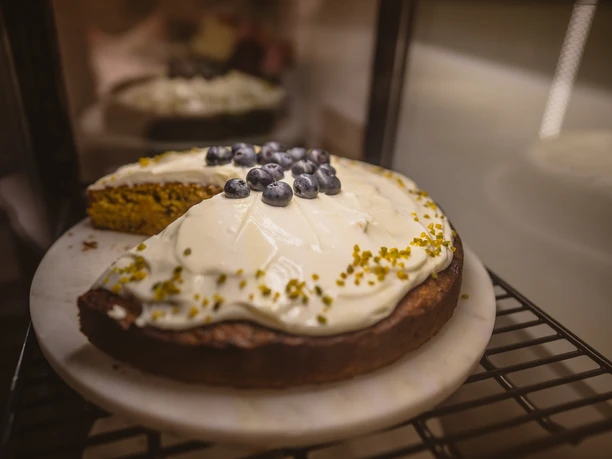 Eine geschnittene Torte mit weißer Creme und Blaubeeren auf einer Kuchenplatte.