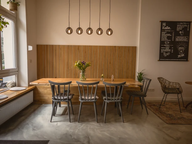 <p>Gemütliches Café mit Holztisch, buntem Blumenstrauß, modernen Lampen und stilvollen Stühlen.</p>