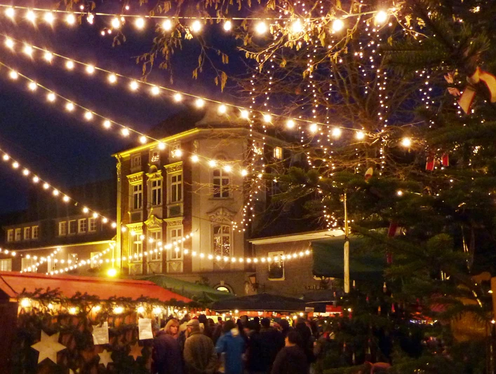 Blotschenmarkt-in-Mettmann-Titelbild.jpg Nächtlicher Weihnachtsmarkt in Mettmann mit festlicher Beleuchtung und einem dekorierten Tannenbaum.