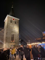 Weihnachtsmarkt2021_Platz Am Offers_StadtVelbert_Schuster_image00036.jpeg Menschen genießen den Weihnachtsmarkt rund um eine beleuchtete Kirche mit Turm im Abendlicht.