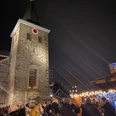 Weihnachtsmarkt2021_Platz Am Offers_StadtVelbert_Schuster_image00036.jpeg Menschen genießen den Weihnachtsmarkt rund um eine beleuchtete Kirche mit Turm im Abendlicht.