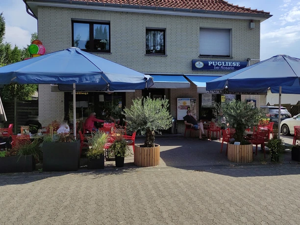 Eiscafé Pugliese mit blauen Sonnenschirmen, roten Tischen und Pflanzen auf der Terrasse an einem sonnigen Tag.