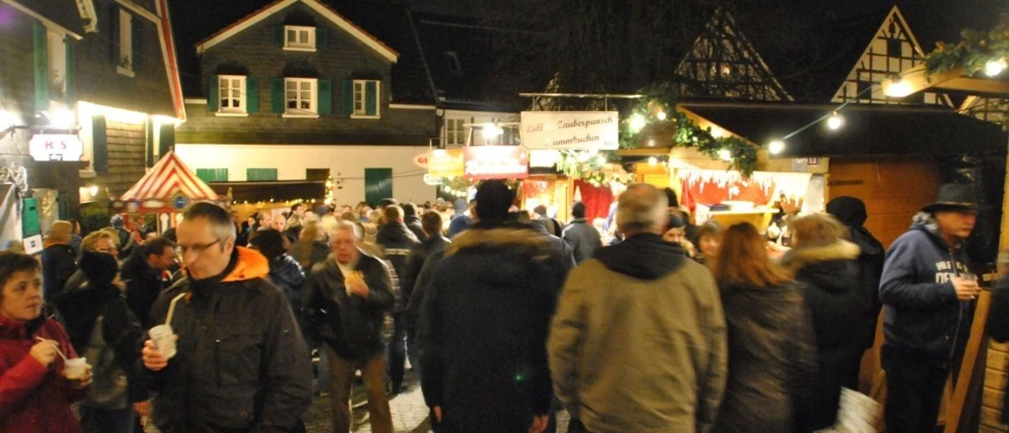 Weinachtsmarkt Wülfrath Titelbild.jpg Nachtaufnahme eines belebten Weihnachtsmarktes in Wülfrath mit zahlreichen Besucher*innen und Lichtern.