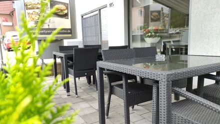 Außenbereich Hemeier Ein moderner Außenbereich mit geflochtenen Gartenmöbeln und Glastischen, umgeben von grünen Pflanzen.