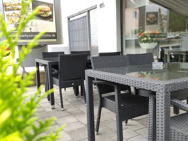 Außenbereich Hemeier Ein moderner Außenbereich mit geflochtenen Gartenmöbeln und Glastischen, umgeben von grünen Pflanzen.