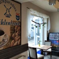 Innenansicht einer Bäckerei mit einem Tisch, Kaffeeautomat und einem dekorativen Wandbild mit Logo.