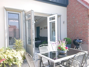 Ein gemütlicher und einladender Essbereich im Freien mit modernen Gartenmöbeln und blühenden Pflanzen.A cozy and inviting outdoor dining area with modern garden furniture and flowering plants.Et hyggeligt og indbydende udendørs spiseområde med moderne havemøbler og blomstrende planter.Een gezellige en uitnodigende eethoek buiten met modern tuinmeubilair en bloeiende planten.