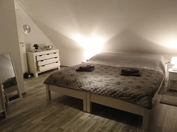 Dachgeschoss-Schlafzimmer mit Doppelbett und Nachttischen, sanfte Beleuchtung verleiht warme Atmosphäre.Attic bedroom with double bed and bedside tables, soft lighting creates a warm atmosphere.Soveværelse på loftet med dobbeltseng og natborde, dæmpet belysning skaber en varm atmosfære.Zolderslaapkamer met tweepersoonsbed en nachtkastjes, zachte verlichting zorgt voor een warme sfeer.