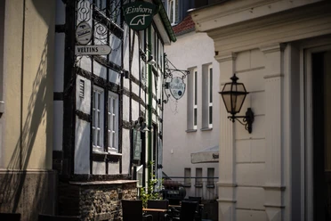 Fachwerkhaus in schmaler Gasse mit Laterne und Gasthofschildern in gemütlicher Atmosphäre.