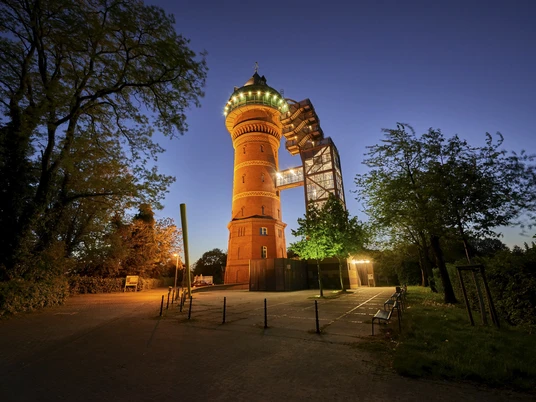 Aquarius, Mülheim an der Ruhr Beleuchteter historischer Wasserturm (heute Aquarius) bei Nacht, umgeben von Bäumen und klarem Himmel