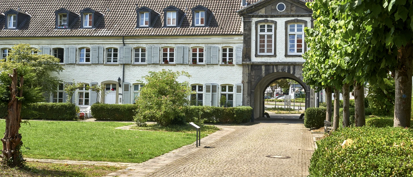 Kloster Saarn, Mülheim an der Ruhr Gebäude mit Arkadenbögen, weißen Fassaden und gepflegtem Grün im Vordergrund.