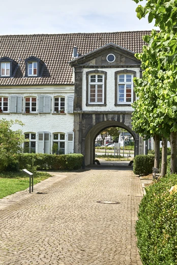 Kloster Saarn, Mülheim an der Ruhr Gebäude mit Arkadenbögen, weißen Fassaden und gepflegtem Grün im Vordergrund.