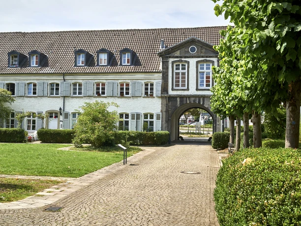 Kloster Saarn, Mülheim an der Ruhr Gebäude mit Arkadenbögen, weißen Fassaden und gepflegtem Grün im Vordergrund.
