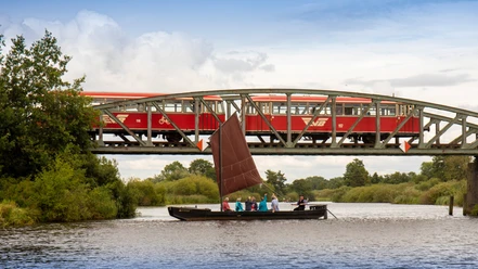 Een turfschip vaart op de Hamme voor de spoorbrug, waar de Moorexpress oversteekt.