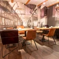 Möbelei Restaurant mit Industriecharme: Verschiedene Stühle, Holztische, große Fototapete einer Fabrik.