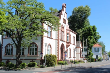 Rathaus von Erkrath Historisches Gebäude mit neugotischen Elementen, rotem Ziegelstein und Bäumen im Hintergrund.