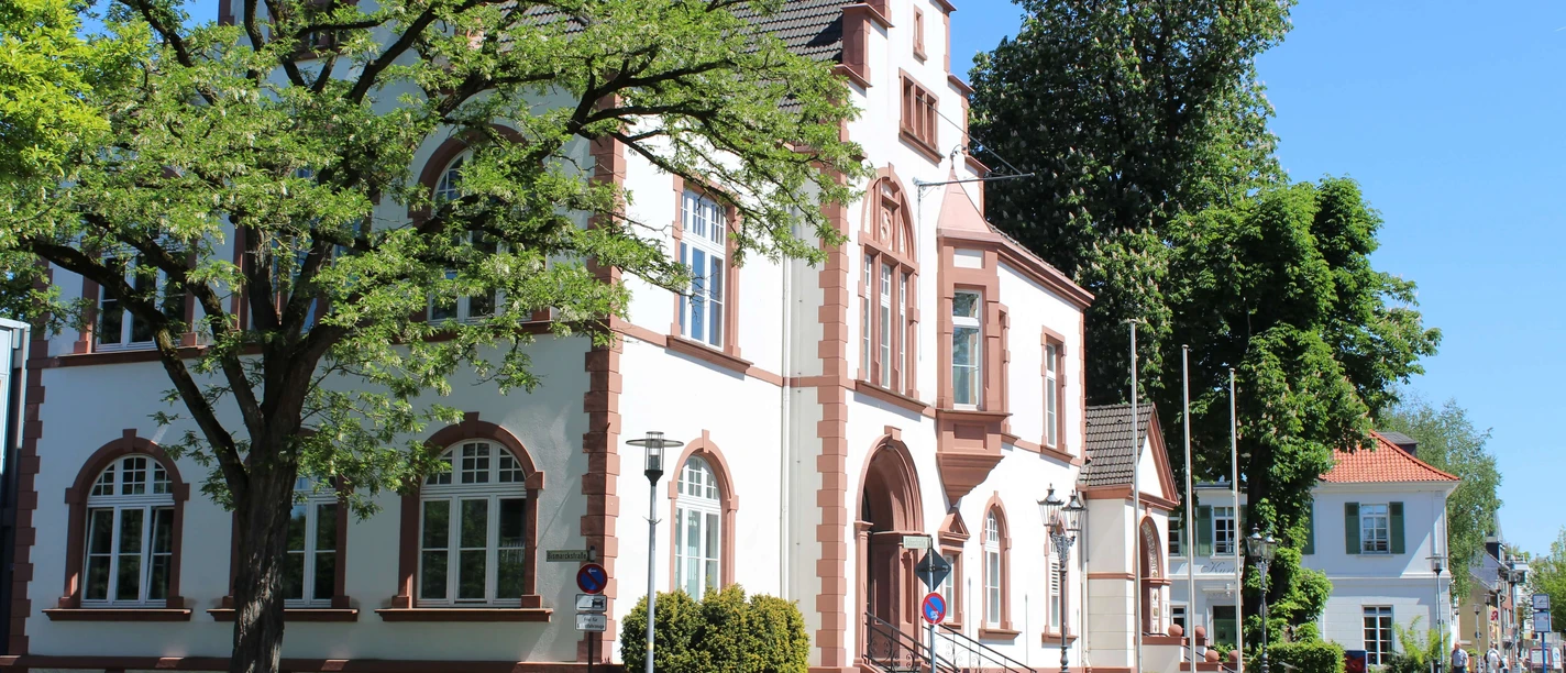 Rathaus von Erkrath Historisches Gebäude mit neugotischen Elementen, rotem Ziegelstein und Bäumen im Hintergrund.