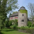 Wasserburg Haus zum Haus in Ratingen Wasserburg inmitten grüner Landschaft, umgeben von Wassergraben und bewachsenen Mauern aus Naturstein.