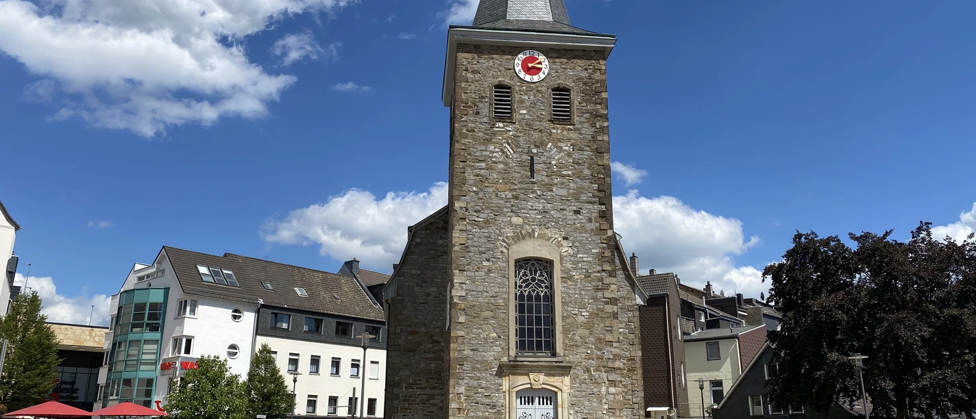 Alte Kirche in Velbert Alte Kirche in Velbert mit steilem Turm und Uhr, umgeben von modernen Gebäuden und blauem Himmel.