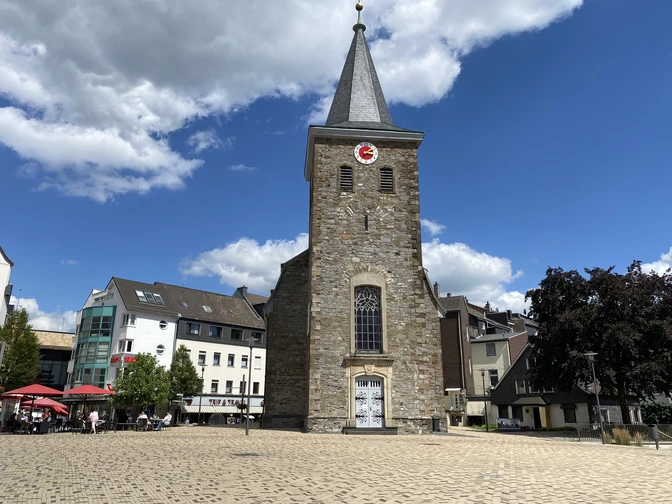 Alte Kirche in Velbert Alte Kirche in Velbert mit steilem Turm und Uhr, umgeben von modernen Gebäuden und blauem Himmel.