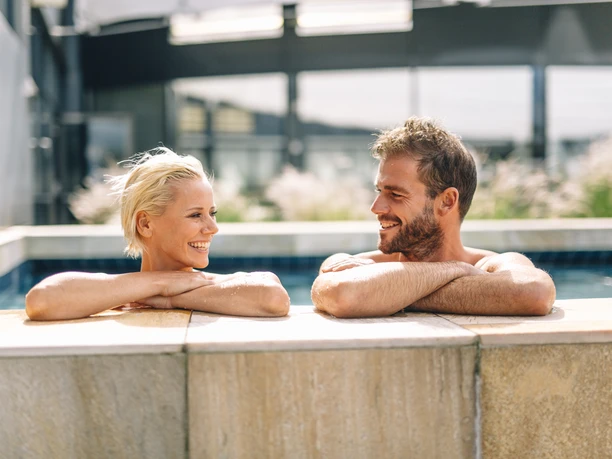 Ishara: Buitenzwembad Zwei Personen lachen sich in einem Außenbecken an, während sie am Beckenrand lehnen.