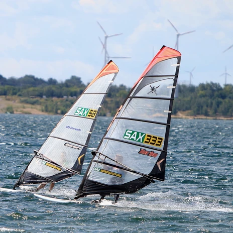 Windsurfer on Lake Zwenkau, gliding in strong winds in front of wind turbines on the shore horizon.