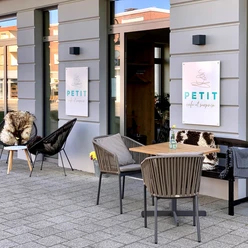 Petit_Denis_1.jpg Gemütliches Außencafé mit Holztischen und Stühlen, das einen einladenden Eindruck vermittelt.