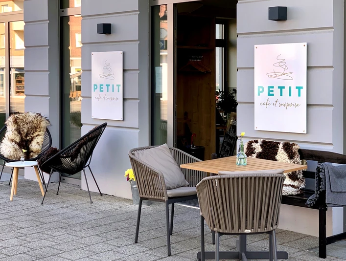 Petit_Denis_1.jpg Gemütliches Außencafé mit Holztischen und Stühlen, das einen einladenden Eindruck vermittelt.