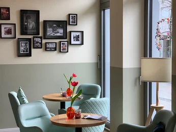 Gemütliches Café mit mintfarbenen Sesseln, runden Holztischen und Fotos an pastellfarbenen Wänden.