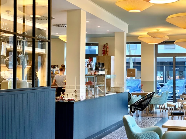 Ein modernes Café mit hellen Lampen, gemütlichen Sitzgelegenheiten und einem einladenden Thekenbereich.