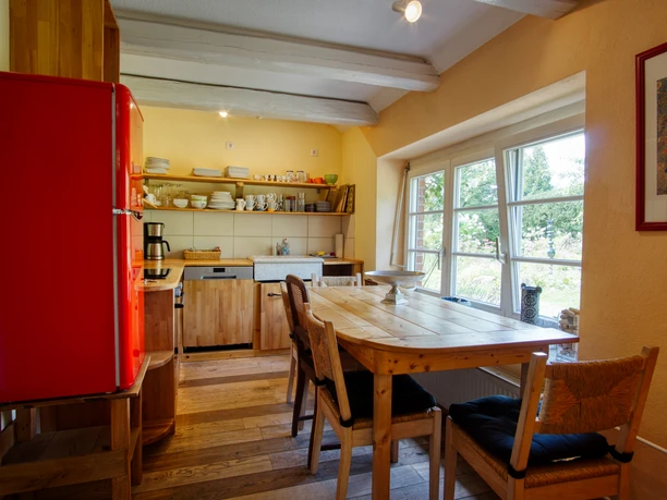 Küche mit rotem Kühlschrank, Holztisch, Stühlen und einem Fenster mit Blick in den Garten.