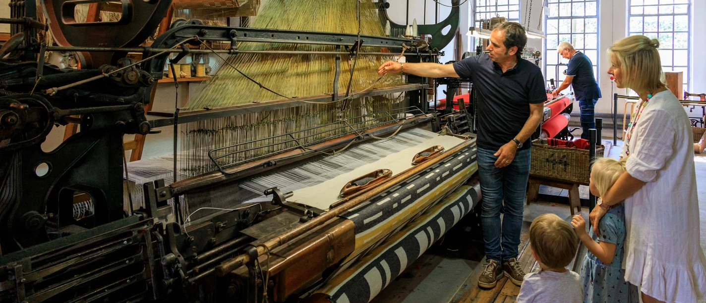 Führung an laufenden Maschinen Historical weaving machine with a group of visitors, including adults and children, in a museum.