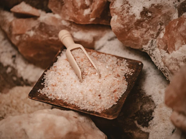 Natürliches Salz in einer Holzschale mit kleiner Schaufel, umgeben von größeren Salzkristallen.