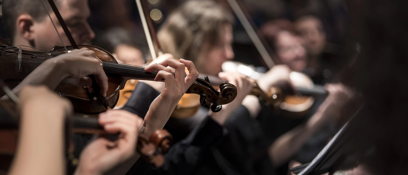 Nahaufnahme eines Sinfonieorchesters in Aktion, Geiger konzentriert beim Spielen, warme Beleuchtung.